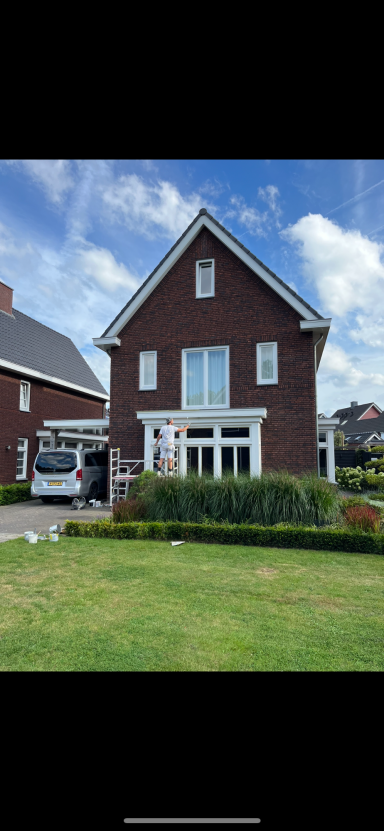 Twee verdiepingen tellend bruin huis met witte ramen en een groene tuin.