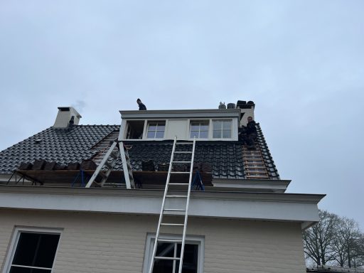 Dakkapel op een huis met ladder en bouwers bezig met reparaties aan het dak.